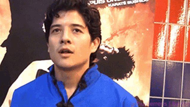 a man in a blue shirt stands in front of a karate poster