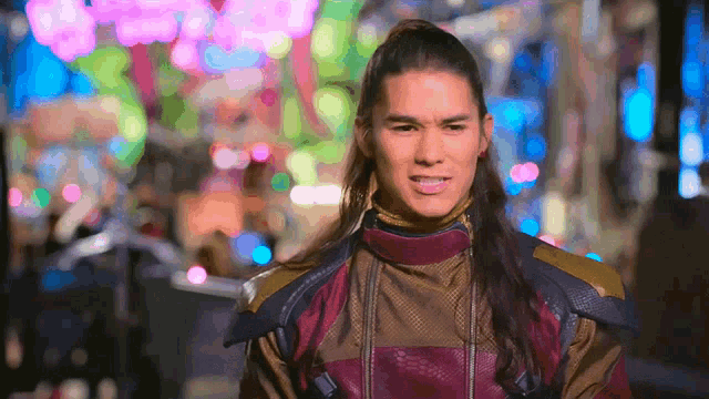 a man with long hair is standing in front of a blurred background