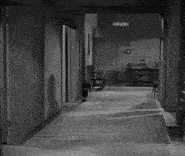 a black and white photo of a man and a woman walking down a hallway with a sign on the wall that says " exit "