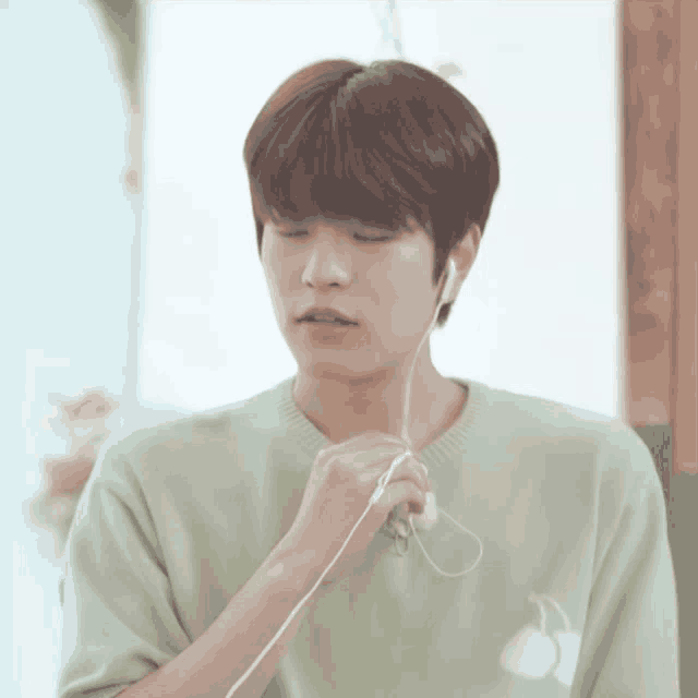 a young man wearing a green sweater is listening to music
