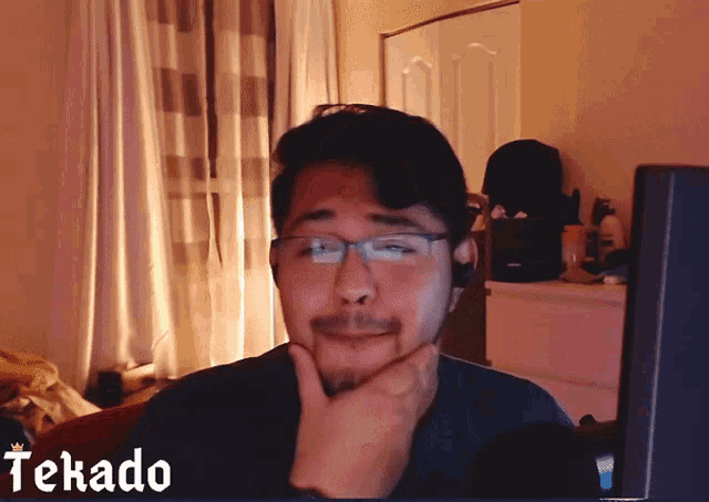 a man wearing glasses and a headset is sitting in front of a screen that says tekada