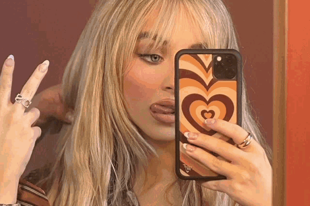 a woman taking a picture of herself with a phone case with a heart on it