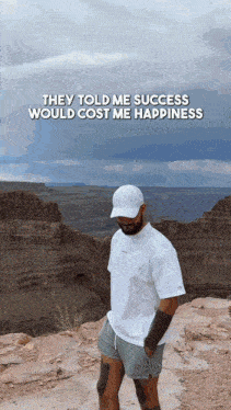 a man standing on top of a rocky hill with the words they told me success would cost me happiness above him .