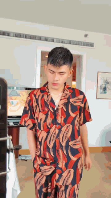 a young man in a colorful shirt and pants is standing in a room with his hands in his pockets