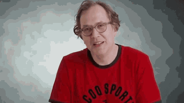 a man wearing glasses and a red shirt that says coq sportif on it