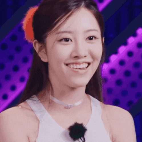 a woman wearing a white tank top and a choker smiles in front of a purple background