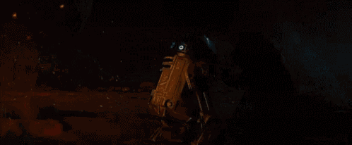 a person is standing next to a r2d2 robot in the dark .