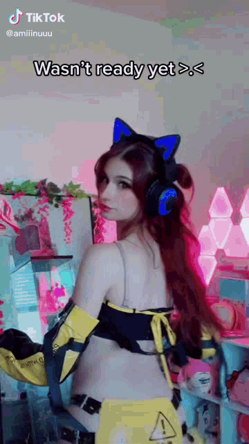 a woman wearing headphones and a bikini top is standing in a room with a pink light behind her .