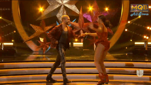 a man and a woman are dancing on a stage in front of a sign that says mqbe