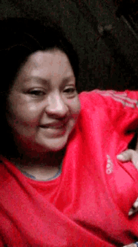 a woman wearing a red adidas shirt is smiling and holding her breast .
