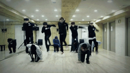 a group of people are jumping in the air in a dance studio with the letter k on the wall behind them