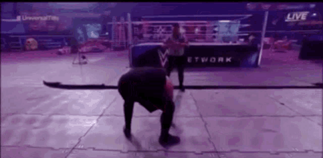 a man is kneeling on the floor in a wrestling ring during a live broadcast .