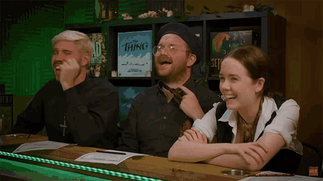 three people are sitting at a table with a sign that says " the thing "