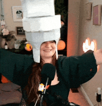 a woman wearing a hat made out of toilet paper is standing in front of a microphone