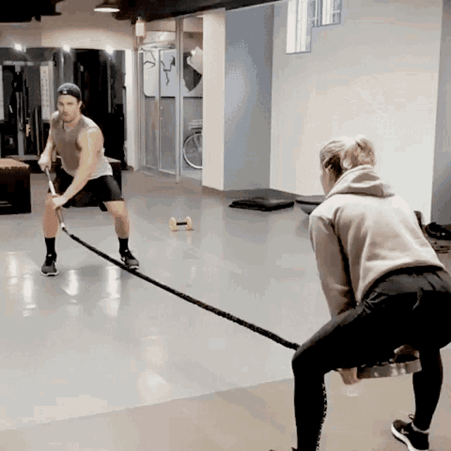 a man is pulling a rope in a gym while a woman sits on a bench