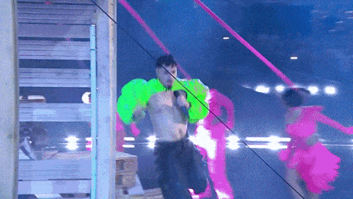 a man without a shirt is singing into a microphone with neon green wings