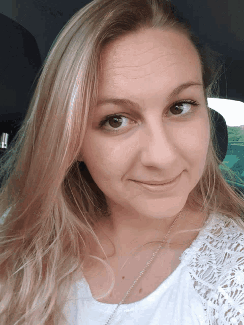 a woman wearing a white lace top is smiling for the camera