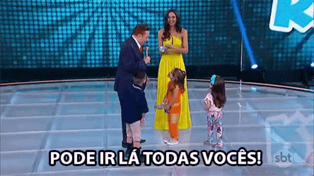 a group of children are standing on a stage with a woman in a yellow dress .