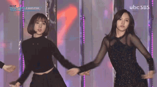 two women are dancing on a stage with ubc sbs written on the bottom right