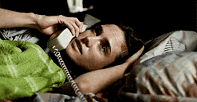 a man is laying in bed talking on a telephone