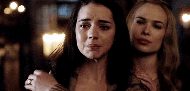 two women are standing next to each other , one is crying and the other is holding her shoulder .