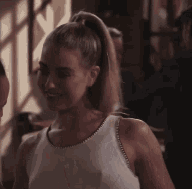 a woman in a white tank top with a ponytail