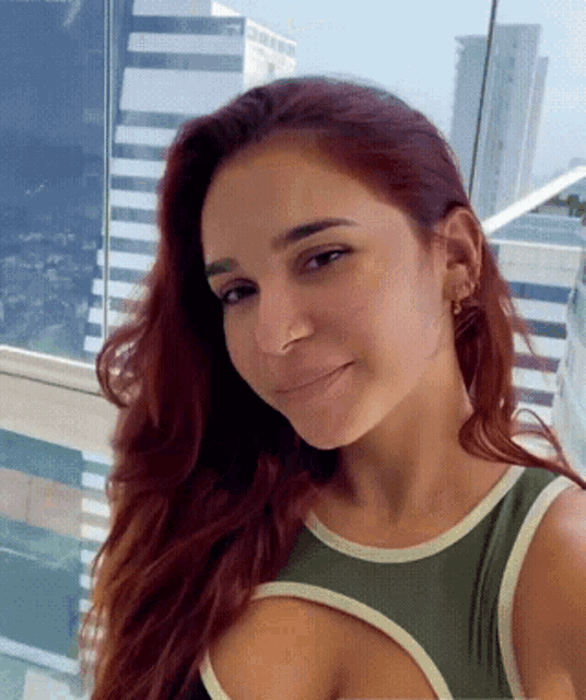 a woman with red hair and a green tank top smiles for the camera