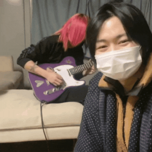 a man with pink hair is playing a purple guitar next to a woman wearing a mask