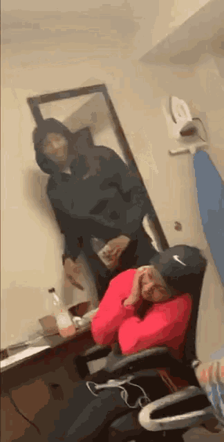 a man in a hoodie is standing next to a woman sitting in a chair in a room .