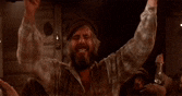 a man with a beard is raising his arms in the air in a room .