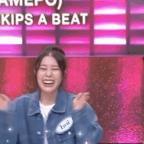 a woman in a denim jacket is laughing in front of a pink background that says kips a beat .