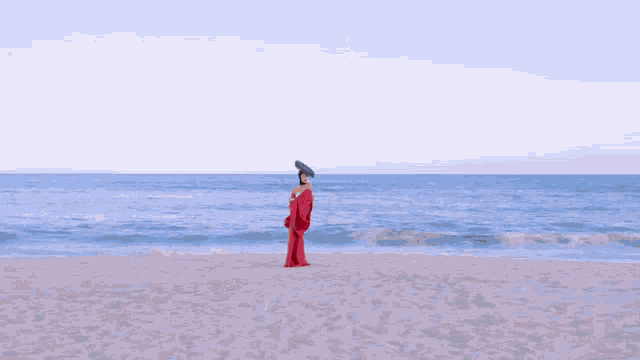 a woman in a red dress is standing on a beach with the ocean in the background