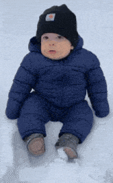 a baby wearing a carhartt hat and a blue jacket is sitting in the snow