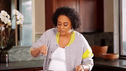 a pregnant woman is cooking in a kitchen while wearing a baseball jacket .