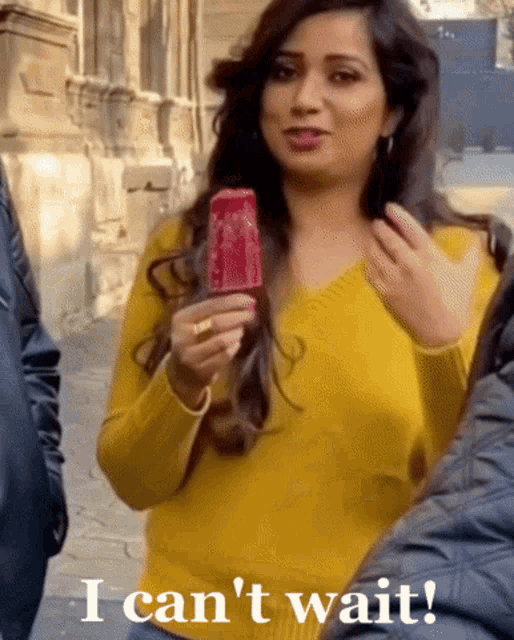 a woman in a yellow sweater is holding a red popsicle and says " i can 't wait " below her