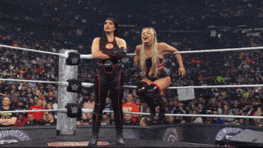 two women are standing in a wrestling ring with a w on the ropes