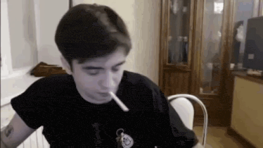 a man is smoking a cigarette while sitting at a table in a room .