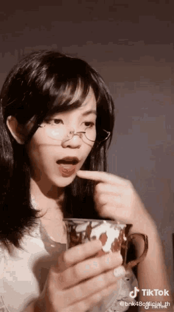 a woman wearing glasses is holding a cup of tea .