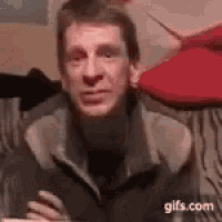 a man in a jacket is sitting on a couch with his arms crossed .