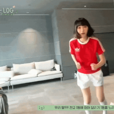 a girl in a red adidas shirt and white shorts is dancing in a living room