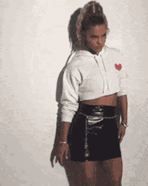a woman in a white crop top and black skirt is standing in front of a white wall