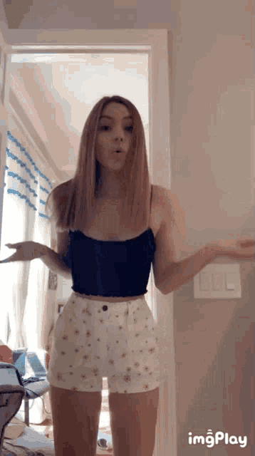 a woman in a black tank top and white shorts is standing in a room .