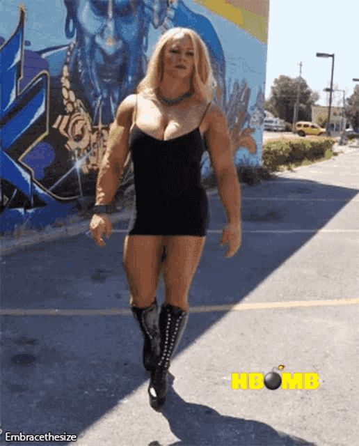a woman in a black dress is walking in front of a wall with graffiti on it that says hbomb on it