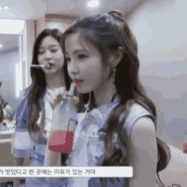 two girls are standing next to each other and one is holding a bottle of red liquid .
