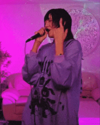 a person is singing into a microphone while wearing a purple shirt .