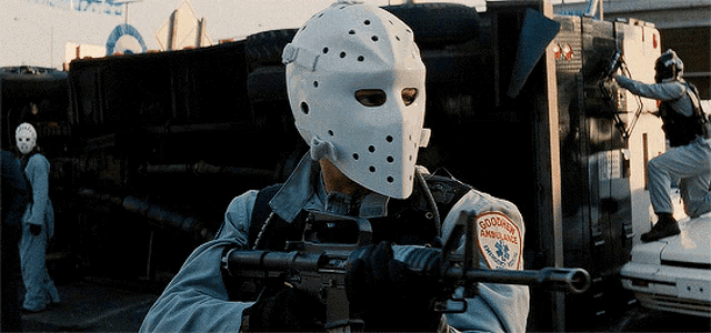a man wearing a hockey mask is holding a gun and has a patch on his sleeve that says emergency ambulance
