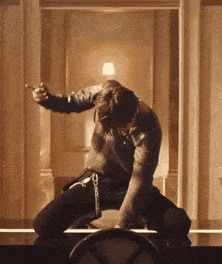 a man in a leather jacket is kneeling on a table holding a cigarette