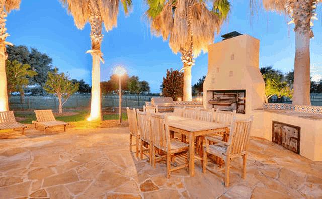 a patio with a table and chairs and a fireplace surrounded by palm trees