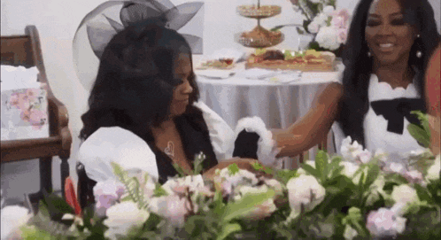 two women are sitting at a table surrounded by flowers .