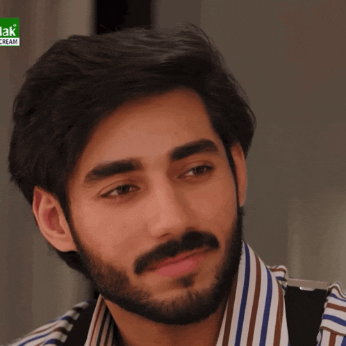 a man with a beard is wearing a striped shirt with a jak cream logo behind him